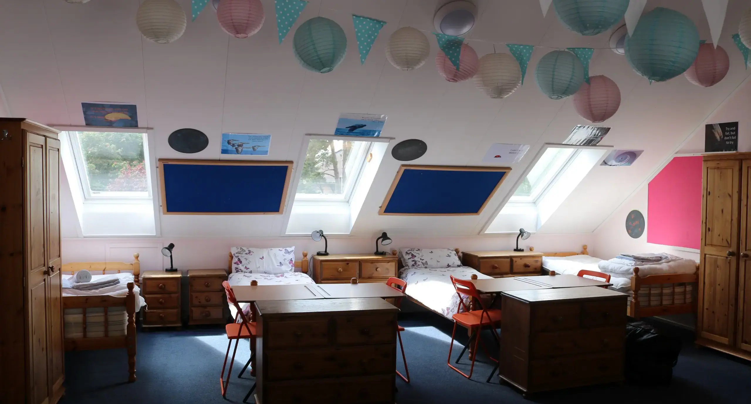 Interior of a boarding school bedroom, with several beds and bedside tables