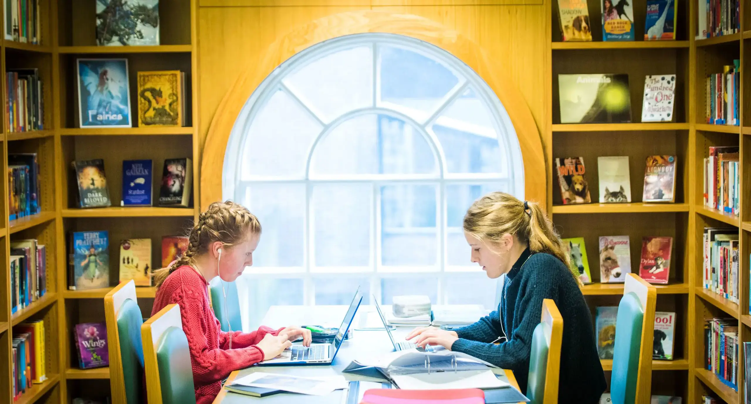 Two pupils studying in a library, in front of a large round window